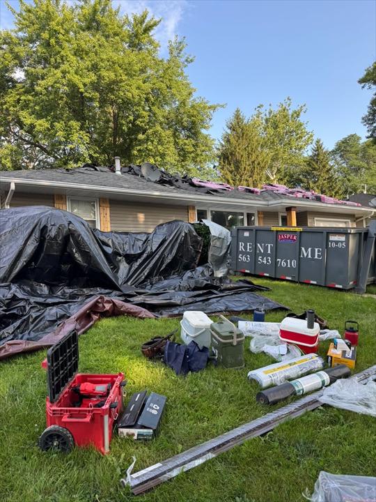 Tarps protecting landscaping and a dumpster staged beside a house during a roof tear-off