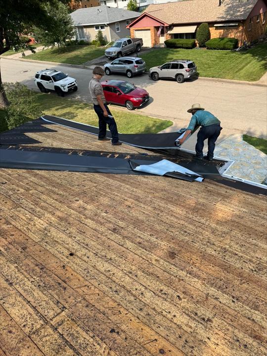 Two roofers rolling synthetic underlayment across bare roof decking