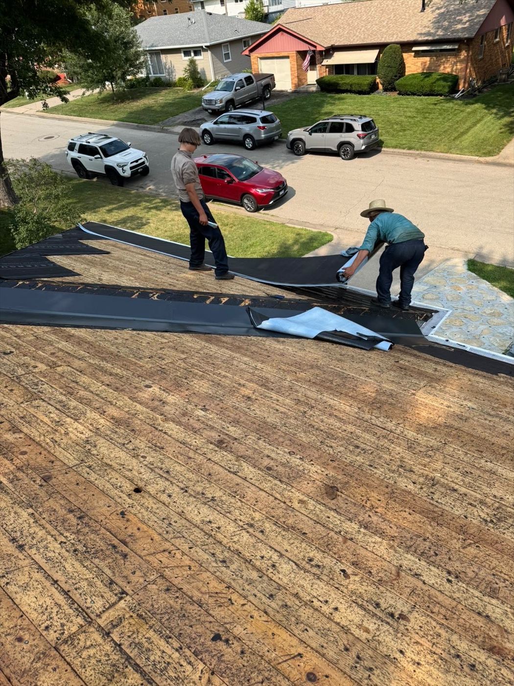 Two roofers rolling out synthetic underlayment across a stripped roof deck